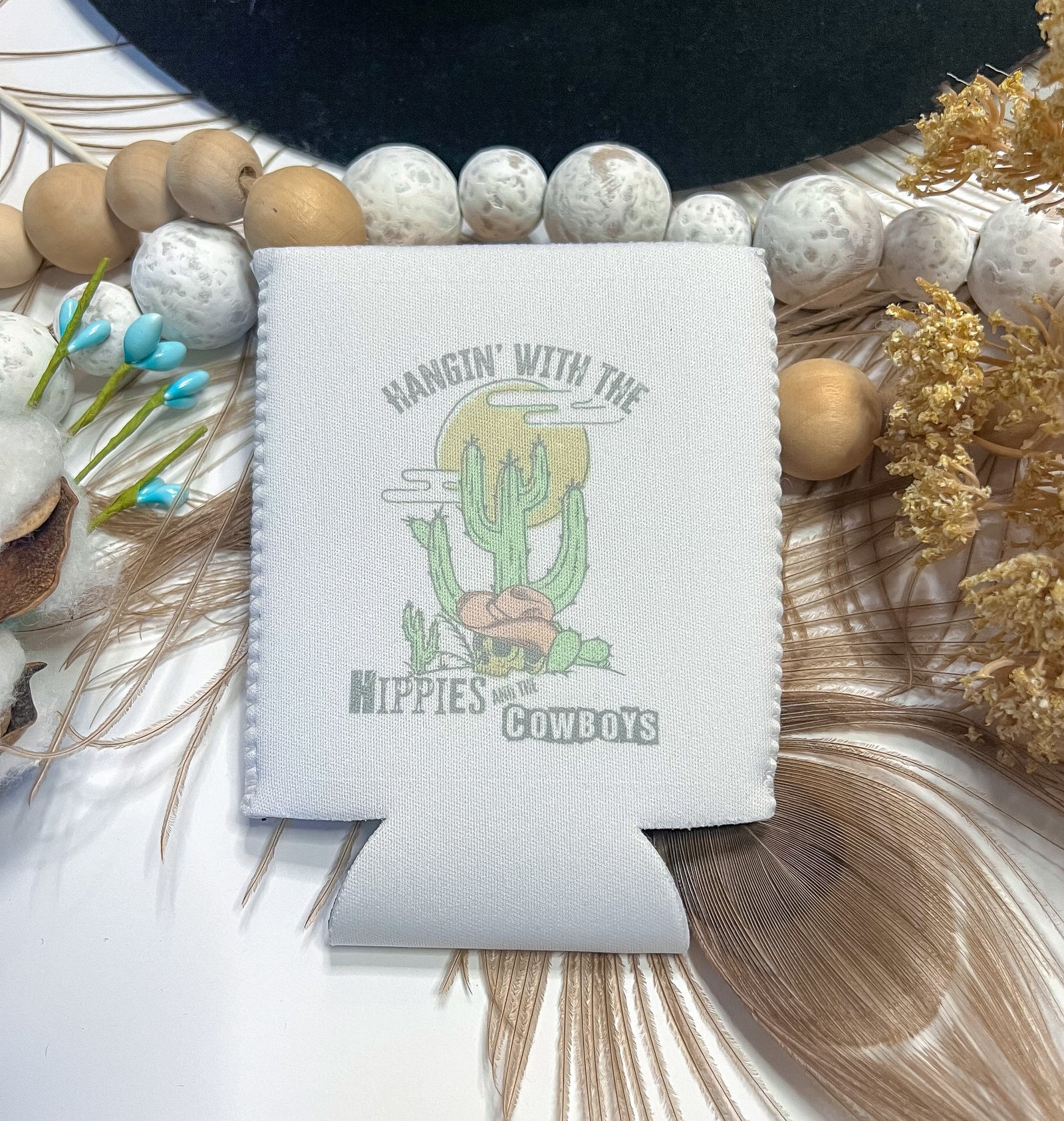 Pictured is white koozie that says hangin' with the hippies and the cowboys.