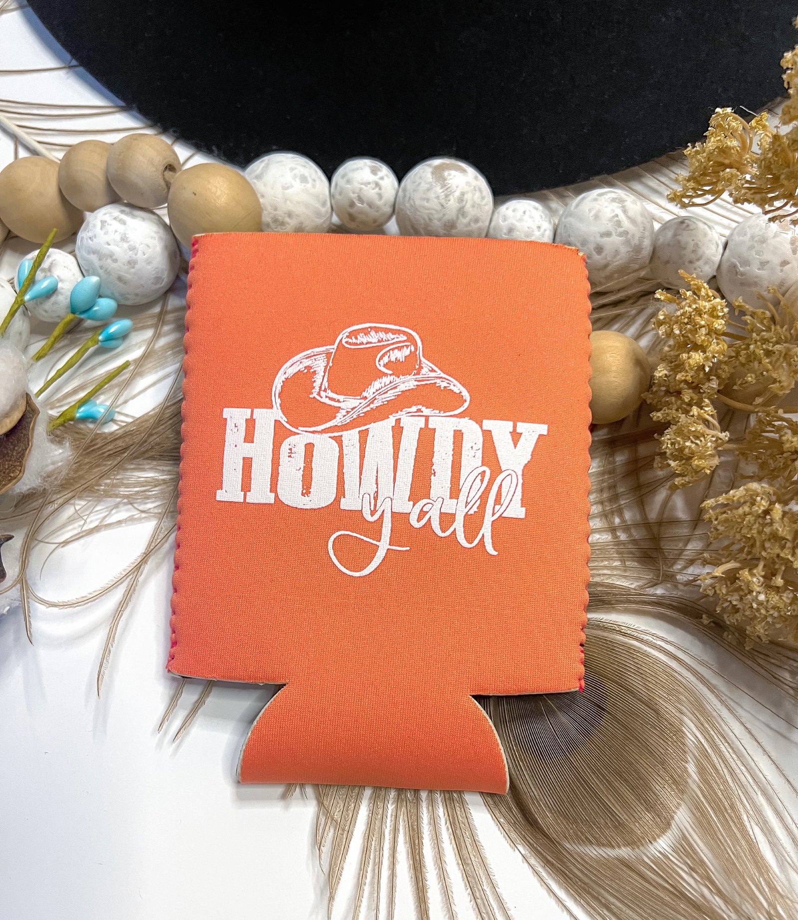 Pictured is a coral koozie that says howdy y'all.