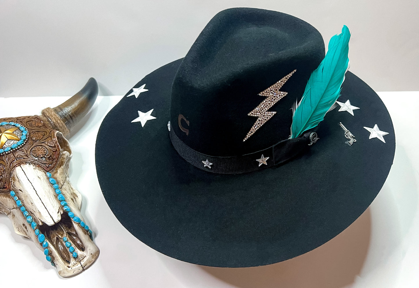 Pictured is a black felt hat with 4 white stars, rhinestone lightning bolt, and teal feathers.