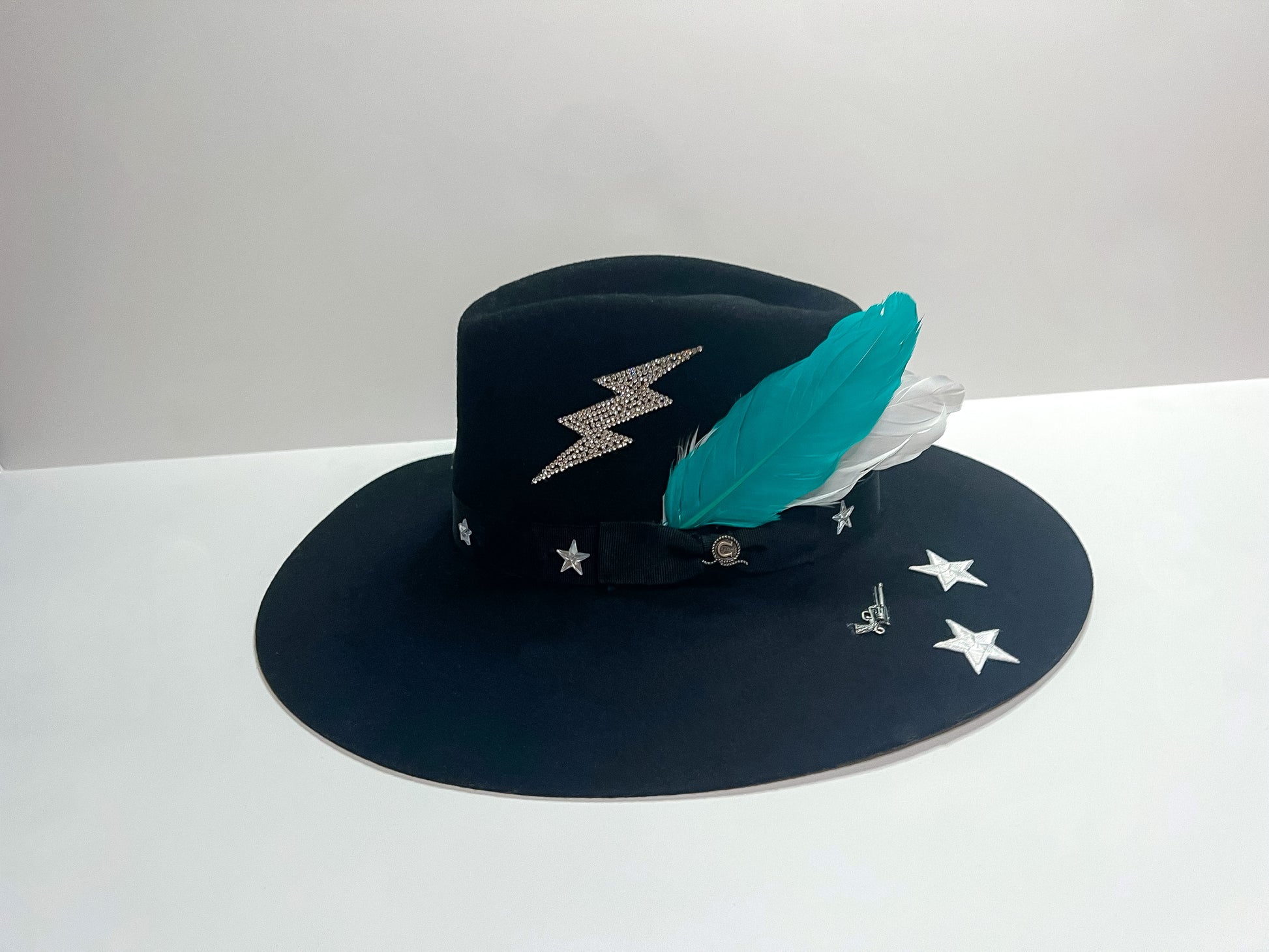 Pictured is a black felt hat with 4 white stars, rhinestone lightning bolt, and teal feathers.